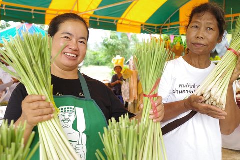 Two women holding bunches of lemongrass at a market stall in Kuiburi